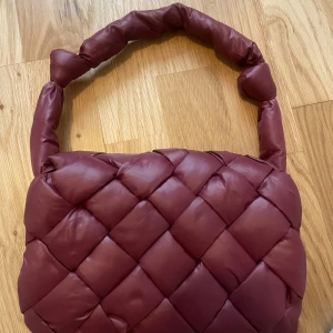 Vinröd vadderad axelväska med flätat mönster - Helt oanvänd trendig vinröd axelväska med vadderat och flätat mönster på framsidan. Väskan har ett tjockt, tvinnat axelband och flera innerfack, inklusive ett med dragkedja. Perfekt för att bära dina viktigaste saker med stil.  💞💞💞