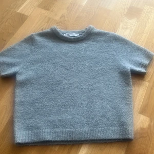 Stickad tröja från Zara - Mysig grå stickad tröja från Zara med korta ärmar och rund halsringning. Tröjan har en enkel och stilren design med ribbade kanter nedtill och vid ärmslut. Säljer pågrund av att den inte används då jag har en liknande tröja. Ordinarie pris 249.