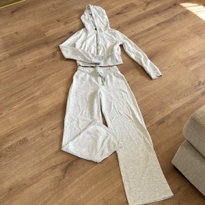 Set från Gina Tricot 🧸 - Säljer ett ljusgrått set med croppad hoodie och matchande vida mjukisbyxor med resår och dragsko i midjan. Köpt på Vinted men har inte använts. 🧸Både hoodien och byxorna är i stl M.