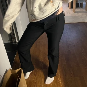 Svarta lågmidjade kostymbyxor med bootcut  - Snygga svarta kostymbyxor med bootcut passform och dragsko i midjan. Byxorna har en klassisk look och är perfekta för en stilren outfit. Materialet känns mjukt och följsamt.