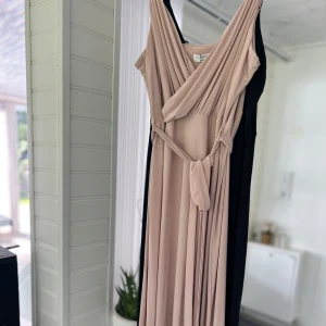 2 st bal klänningar - Säljer en elegant beige & svart omlottklänningar från Goddiva med v-ringning och knyt i midjan. Klänningen har smala axelband och ett fint fall i tyget, perfekt för speciella tillfällen.