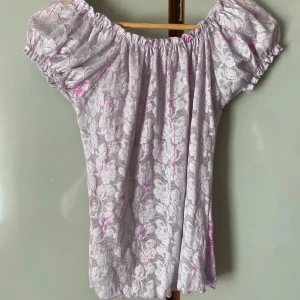Ljuslila offshoulder blus med spets - Säljer en söt ljuslila blus med offshoulder-modell och blommig spets. Blusen har korta puffärmar och ett romantiskt uttryck med transparent spets över ett ljust tyg. Perfekt för vår och sommar!