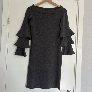 Klänning med volangärmar - Mörkgrå stickad klänning med unika volangdetaljer på ärmarna. Klänningen har en kroppsnära passform och är perfekt att  styla med boots eller sneakers till en utekväll! Storleken är M men passar även mig som är S. Nyskick.