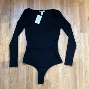 Svart långärmad bodysuit från NLY One - Säljer en svart långärmad bodysuit från NLY One med sweetheart-urringning. Tight passform och stilren design, perfekt att styla till olika outfits. Materialet är mjukt och stretchigt för en bekväm känsla.
