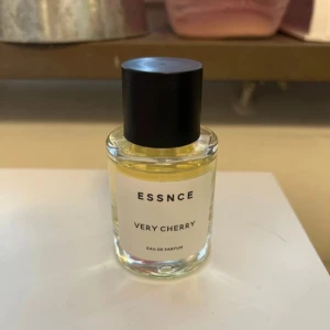 ESSNCE Very Cherry Eau de Parfum - En stilren parfymflaska med svart lock och transparent glas. Doften heter Very Cherry och är en Eau de Parfum från ESSNCE. Minimalistisk design med tydlig etikett framtill.