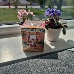 Police To Be Exotic Jungle 40ml - Säljer en parfym Police To Be Exotic Jungle i oöppnad förpackning. Kartongen har tropiskt mönster med blad och en rosa dödskalle på framsidan. Flaskan rymmer 40 ml. Perfekt för dig som gillar unika och färgstarka dofter.