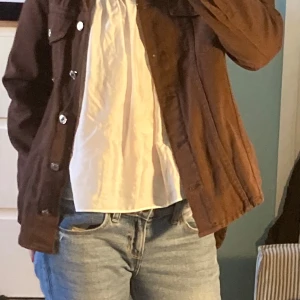 Brun manchesterjacka med silverknappar - Säljer en brun manchesterjacka med klassisk krage och silverfärgade knappar framtill. Jackan har två bröstfickor med lock och knapp, samt raka ärmar. Perfekt för dig som gillar en avslappnad och trendig stil.
