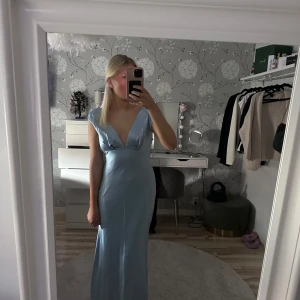 Ljusblå långklänning med djup v-ringning - Säljer en  ljusblå långklänning med djup v-ringning och öppen rygg. Klänningen har en figurnära passform. Perfekt för t.ex balen. Säljes för att den ej var rätt för mig. Aldrig andvänd 