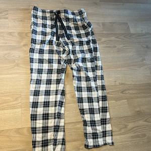 Rutiga byxor från Kappahl - Säljer ett par rutiga byxor från Kappahl i svart, vitt och grått. Byxorna har resår och snörning i midjan för extra komfort. Perfekta för en avslappnad stil och tillverkade i mjukt bomullsmaterial.
