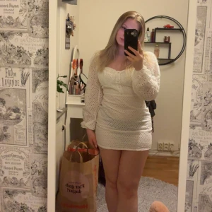 Vit kort klänning med broderade detaljer från Boohoo - Supersöt vit kortklänning från Boohoo med broderade hål och långa puffärmar. Perfekt för sommarens alla tillfällen eller studenten! Aldrig använd och det enda negativa är att den är något genomskinlig vilket framgår på bilden. Säljes då den var för liten för mig. 