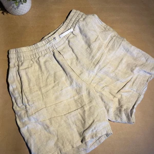 Beiga linneshorts från Weekday - Snygga beiga shorts från Weekday i linne med elastisk midja och avslappnad passform. Perfekta för varma dagar och enkla att matcha med olika toppar. Klassisk design med fickor på sidorna.