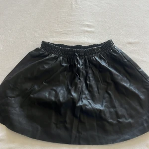Svart kjol i skinnimitation från Zadig & Voltaire - Säljer en svart kortkjol från Zadig & Voltaire i skinnimitation. Kjolen har resår i midjan och knytband. Stilren och lite edgy!! Använd några gånger och är i storlek 14y/S 🌸 