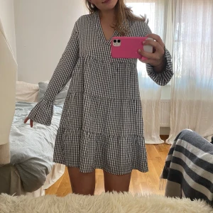 Rutig klänning från NA-KD - Säljer en svartvit rutig klänning från NA-KD i storlek 36. Klänningen har v-ringning, långa ärmar och volangdetaljer nertill. Använd typ 4 gånger. 