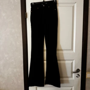 Svarta bootcut jeans - Säljer ett par svarta bootcut jeans. Byxorna har klassisk femficksdesign och stängs med knapp och dragkedja. Perfekta för dig som gillar en retroinspirerad look med utsvängda ben.