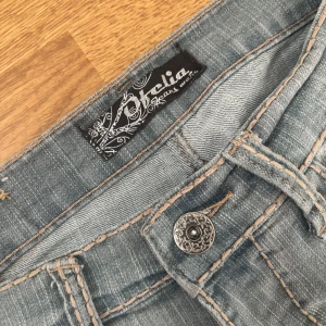 Ljusgrå straightleg jeans - Säljer ett par vintage ljusgrå jeans med dekorativa sömmar. Byxorna har raka ben och snygga detaljer på knappen och bakfickorna.