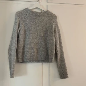 Grå stickad tröja från Vero Moda - Mysig grå stickad tröja från Vero Moda. Tröjan har en klassisk rund halsringning, långa ärmar och ribbade muddar vid ärmslut och nederkant. Perfekt för kyligare dagar och enkel att matcha med olika outfits.❤️