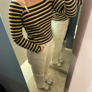 Randig långärmad topp från Monki - Långärmad topp från Monki med svarta, vita och gula ränder. Tröjan har en fyrkantig ringning och är ribbad i materialet.