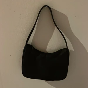 Svart axelväska - En stilren svart axelväska med enkel design och mjuk form. Perfekt för att bära dina viktigaste saker. Väskan har ett klassiskt utseende och passar till många olika outfits.