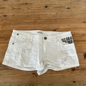 Vita jeansshorts med nitar från Terranova - Snygga vita lågmidjade jeansshorts med slitna detaljer och silvriga nitar på fickan. Klassisk femficksmodell med låg midja och råa kanter. Perfekta för sommaren och ger en cool vibe till din outfit.