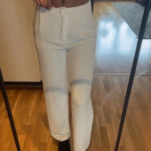 Vita tyg kostymbyxor med dragkedja - Snygga vita tyg kostymbyxor med hög midja och raka ben. Byxorna har dragkedja och knapp framtill för stängning. Perfekta för en clean och stilren look.