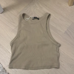 Beige ribbad croppad linnetopp - Säljer en beige croppad linnetopp med ribbad struktur. Perfekt för varma dagar och enkel att matcha med olika outfits. Tidlös och stilren design.