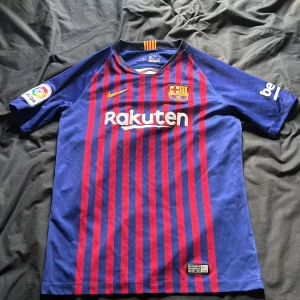 FC Barcelona hemmatröja 2018/2019 - Säljer en officiell FC Barcelona hemmatröja från säsongen 2018/2019. Tröjan är blå med röda vertikala ränder, har korta ärmar och klubbmärke på bröstet. Nike-logga och sponsortryck på framsidan, samt Unicef-tryck på ryggen.