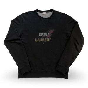 Sweatshirt från Saint Laurent - Cool svart sweatshirt från Saint Laurent med tryckt logga och blixtdetalj på bröstet. Klassisk rund halsringning och långa ärmar. Perfekt för en avslappnad och trendig look.