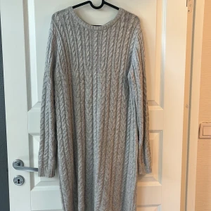 Ljusgrå stickad långklänning från Hampton Republic - Mysig ljusgrå stickad långklänning från Hampton Republic med kabelstickat mönster och rund halsringning. Klänningen har långa ärmar och dragkedja i ryggen. Perfekt för kyligare dagar.