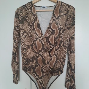 Brun ormmönstrad omlottbody Zara - Säljer en snygg omlottbody från Zara med ormmönster i bruna och beige toner. Djup v-ringning framtill och långa ärmar. Stretchigt material som sitter tight och markerar midjan. Perfekt för dig som vill sticka ut med ett coolt mönster.