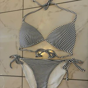 Randig bikini från H&M med knyt - Snygg bikini från H&M med svartvita ränder. Triangelformad överdel med knyt i nacken och ryggen, samt matchande underdel med knyt i sidorna. Underdelen har storlek 34 och överdelen storlek 38.
