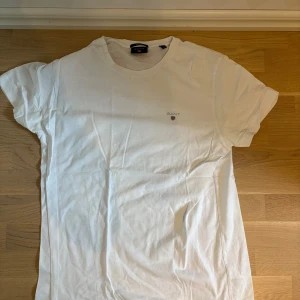 Vit t-shirt från GANT - Klassisk vit t-shirt från GANT med liten broderad logga på bröstet. T-shirten har rund halsringning och korta ärmar. Perfekt basic-plagg i mjuk bomull som funkar till allt.