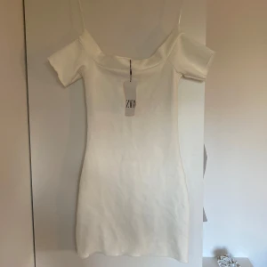 Vit offshoulder klänning från Zara - Helt oanvänd superfin vit kortklänning från Zara med offshoulder. Klänningen har en figurnära passform och är perfekt för sommarens alla tillfällen. Enkel och stilren design som är lätt att matcha. Storlek M men jag skulle säga att den är mer som en S/XS