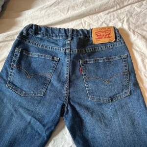 Levi's 511 Slim blå jeans - Säljer ett par klassiska Levi's 511 Slim jeans i blå denim. Byxorna har raka ben, fem fickor och snygga kontrastsömmar. Ikonisk läderpatch bak i midjan och Levi's röda logga på bakfickan. Perfekta för dig som gillar en slim passform och tidlös stil.