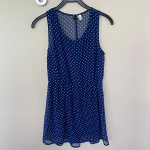 Blå prickig kort klänning H&M - Söt blå kortklänning från H&M med vita prickar. Ärmlös modell med rund halsringning och lätt utställd kjol. Tunt och luftigt material som passar perfekt till varma dagar. Använd fåtal gånger.