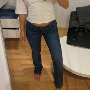 Mörkblå jeans med gul detalj - Säljer ett par mörkblå jeans med snygga kontrastsömmar och unik gul broderad detalj på bakfickan. Jeansen har låg midja och raka ben. Storlek 26/27 