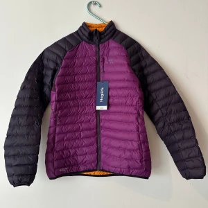 Ny lättviksjacka i lila från Haglöfs strl. s - Essens Mimic Jacket från Haglöfs är en fodrad jacka med bra fukthantering och i vattenavvisande unika material. Isolerad med ett unikt, syntetiskt fodermaterial för bra värme och minimal fuktupptagning Lätt, slitstarkt och vindtåligt 30D DWR-behandlat, fluorkarbonfritt Pertex®-skalmaterial Kortare snitt gör den mindre när den skall packas ner. Axelpartier i stretchfleece för extra rörelsefrihet. 