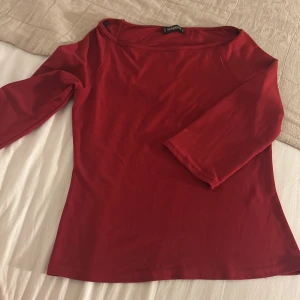 Röd topp - En stilren röd topp med trekvartsärm och rundad halsringning. Modellen är figurnära och enkel, perfekt att matcha med jeans eller kjol. Materialet känns mjukt och stretchigt, vilket gör den bekväm att bära hela dagen.