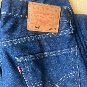 Levi's 501 mörkblå jeans W28 L32 - Klassiska Levi's 501 jeans i mörkblå denim med raka ben och normal passform. Byxorna har fem fickor, knappgylf och den ikoniska läderpatchen bak i midjan. Perfekta för dig som gillar tidlös stil och vill ha ett par schyssta jeans i bomull.