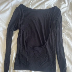 Svart långärmad topp med öppen rygg - Aldrig använd men har inte kvar lapp på.Svart långärmad topp från Gina Tricot i mjuk bomullskänsla. Snyggt djup, öppen rygg som ger en cool och trendig look. Perfekt att styla med jeans eller kjol för en stilren outfit. Enkel och tight passform som sitter snyggt på kroppen.