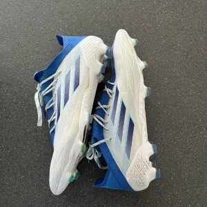  adidas fotbollsskor - Snygga fotbollsskor från adidas i blått och vitt med klassiska tre ränder på sidan. Skorna har snörning, mönstrad sula med dobbar för bra grepp och en sportig design. Ovandelen är i syntetmaterial och mesh för lätt känsla på planen.