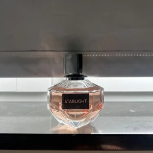 Starlight parfym diamantflaska 100 ml - Säljer en lyxig parfym från Starlight i en snygg diamantformad glasflaska med svart etikett och silverfärgad kork. Doften har en ljusrosa ton som syns genom det klara glaset. Perfekt för dig som gillar eleganta och stilrena parfymer.