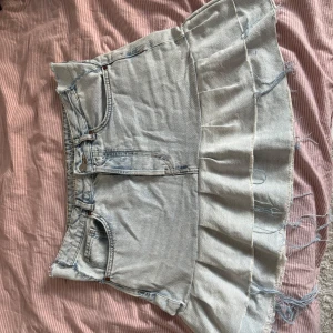 Ljusblå volang jeanskjol - Superfin ljusblå jeanskjol med volangkant och råa, fransiga kanter. Klassisk femficksmodell, egen syd. Kjolen är kort och har en avslappnad vibe, perfekt till sneakers eller boots.