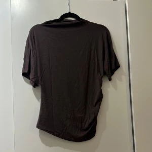 Brun kortärmad topp - En brun topp i mjukt material med korta ärmar och snygg rynkdetalj på ena sidan. 
