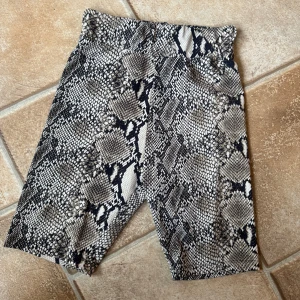 Cykelbyxor med Ormskinnsmönster från Slay   - Snygga shorts från Stay i ormskinnsmönster med svart, grå och beige ton. Modellen är tight och midwaist, perfekta för dig som vill sticka ut. Materialet är stretchigt syntet som sitter skönt mot kroppen. Perfekt till sommarens alla outfits! Sparsamt använda 