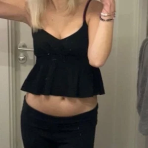 Svart volangtop  - Supersöt svart topp från SHEIN med smala axelband och volang nertill. Toppen har v-ringning och smockad midja som ger en snygg passform. Perfekt att styla med jeans eller kjol för en trendig look.