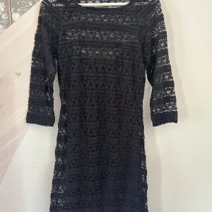 Svart spetsklänning från Lindex - Snygg svart kortklänning från Lindex i spets med trekvartsärm. Klänningen har ett genomgående spetsmönster och sitter figurnära. Perfekt för dig som vill ha en stilren och elegant look.