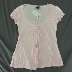 Ljusrosa spetsdetaljerad topp Gina Tricot - Supersöt ljusrosa topp från Gina Tricot med v-ringning, spetskant och rynk framtill. Korta ärmar med volangkant och mjukt, stretchigt material. Perfekt för dig som gillar romantiska vibes och pastellfärger.