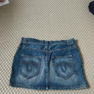 Jeanskjol mini - Säljer en klassisk blå jeanskjol med fem fickor och bälteshällor. Kjolen är kort och har snygga detaljer på bakfickorna med kontrastsömmar. Perfekt till sneakers eller boots för en chill look. Storlek L men skulle säga mer som M. En söm som är lite uttöjd se sista bilden. 