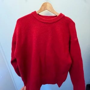 Röd stickad tröja med rund hals - En enkel och snygg röd stickad tröja med rund halsringning och långa ärmar. Perfekt att slänga på sig när det är kyligt ute. Tröjan har en klassisk passform och ribbade muddar vid hals, ärmslut och nederkant.