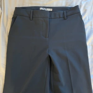 Mörkgrå kostymbyxor från NA-KD - Snygga mörkgrå kostymbyxor från NA-KD med raka ben, hällor för bälte och diskreta fickor både fram och bak. Byxorna har en klassisk look och är tillverkade i ett slätt material som ger en stilren vibe.